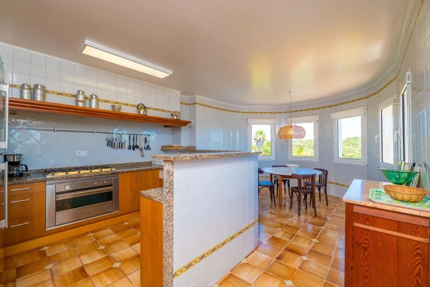 Una cocina luminosa con comedor, una isla alicatada y una mesa de madera.
