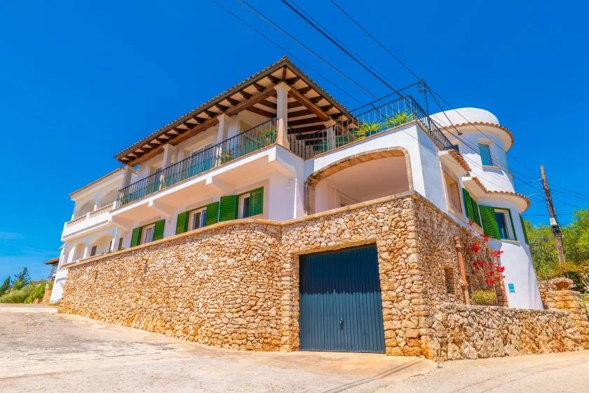 Una casa de varios niveles con muros de piedra, balcones y una gran puerta de garaje oscura.