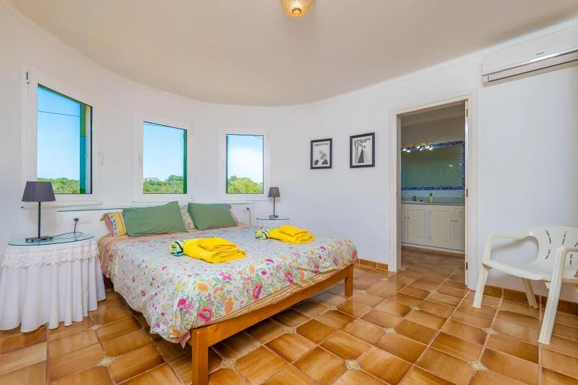 Un dormitorio con una cama cubierta con estampado floral, ventanas y una puerta abierta.