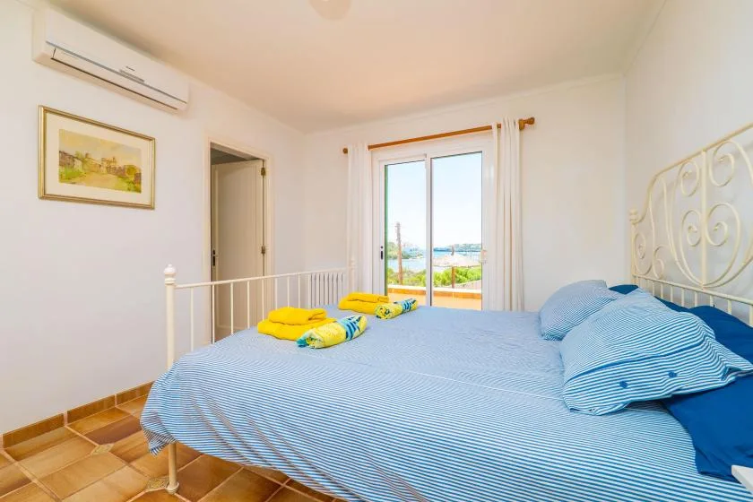 Un dormitorio con ropa de cama a rayas azules y puertas de vidrio que dan a un balcón.