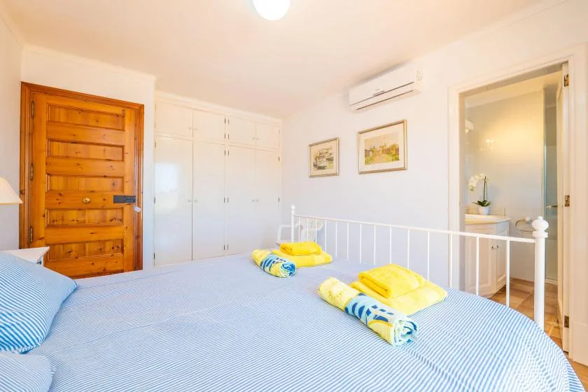 Un dormitorio luminoso con una cama, armarios blancos y una puerta abierta.