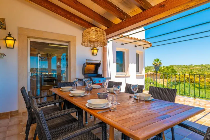 Un comedor exterior cubierto tiene una mesa de madera y vistas a la vegetación.