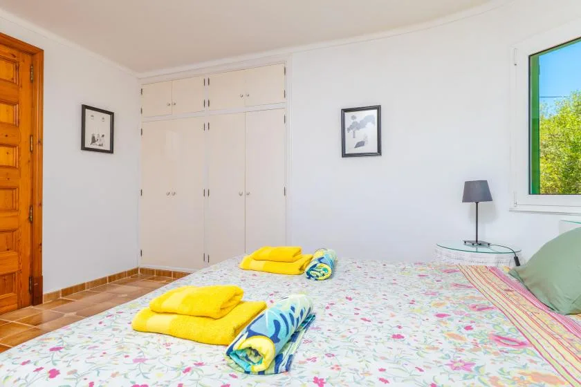 Un dormitorio con una cama, toallas dobladas, armarios empotrados y una ventana.