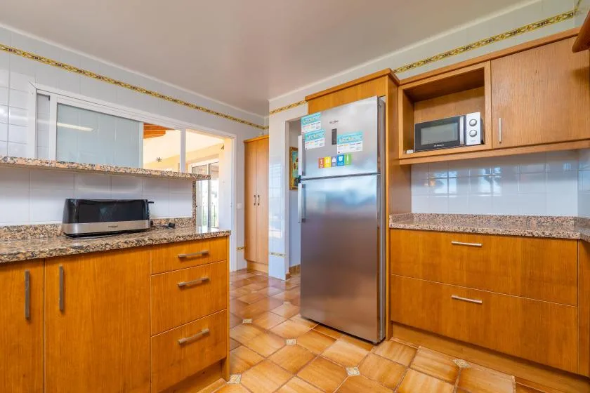 Una cocina con gabinetes de madera, un refrigerador y un microondas sobre la encimera.