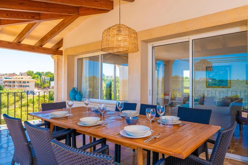 Una zona de comedor exterior cubierta con una mesa larga de madera junto a puertas de vidrio.