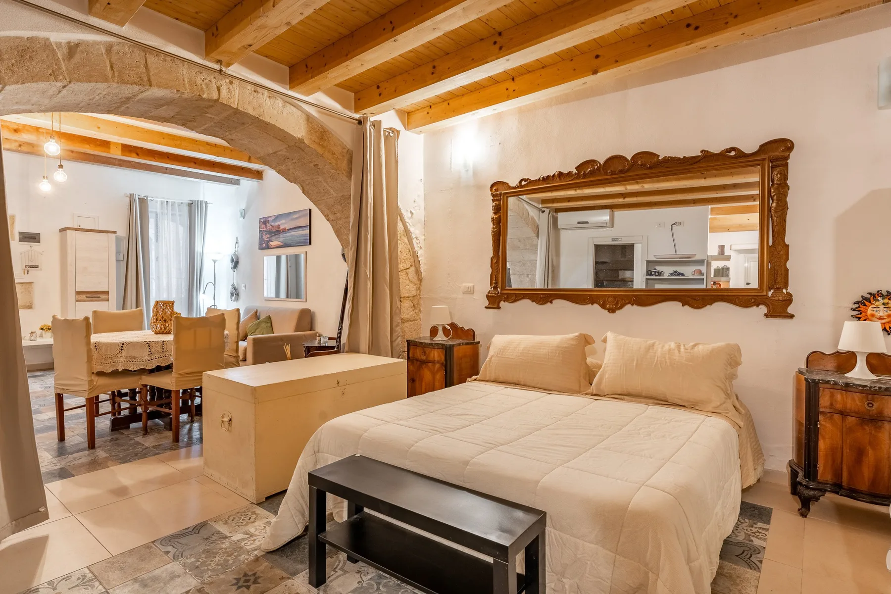 Un dormitorio con una cama bajo un gran espejo ornamentado y vigas de madera a la vista.
