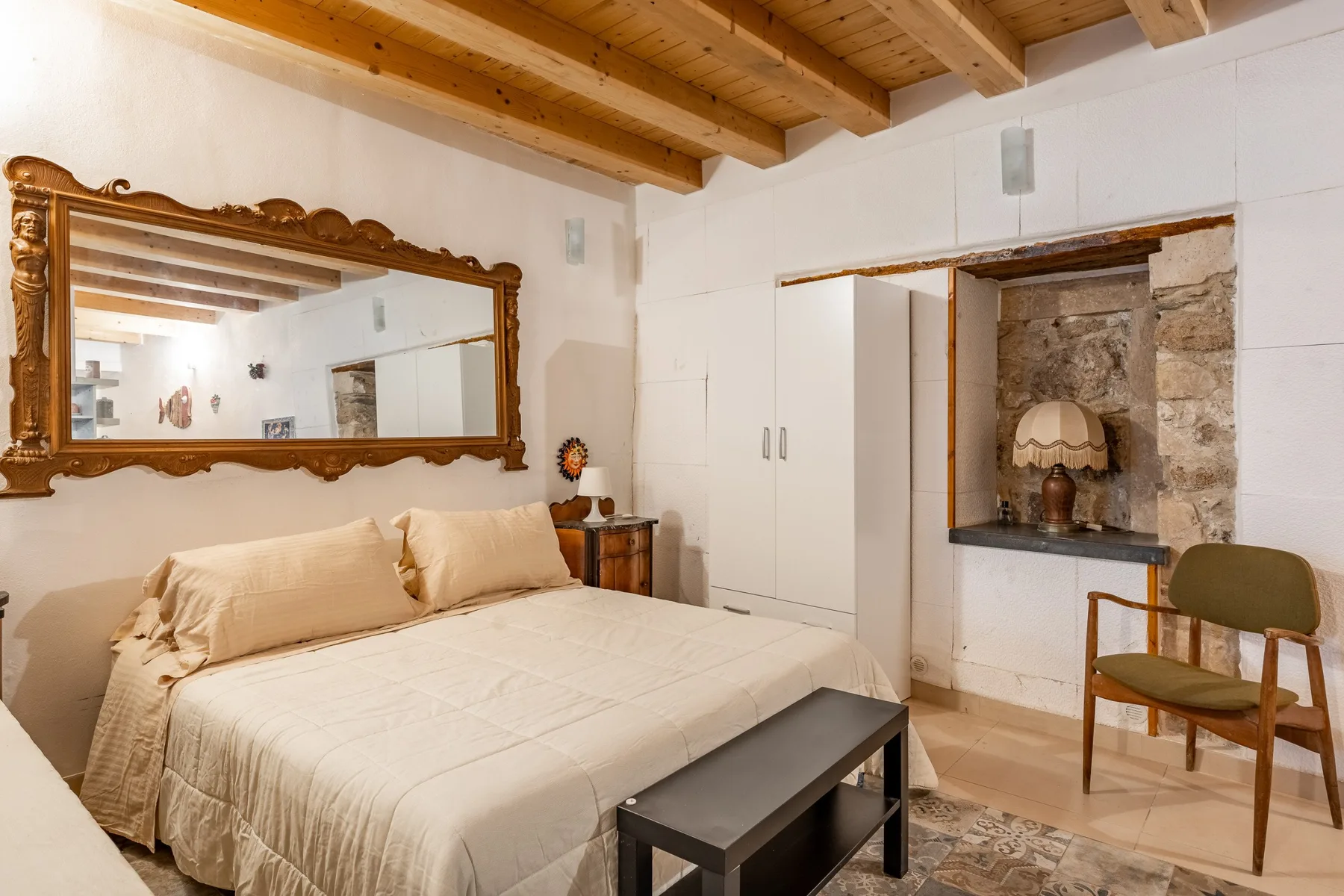 Un dormitorio con una cama grande, un espejo en la pared y vigas de madera a la vista.