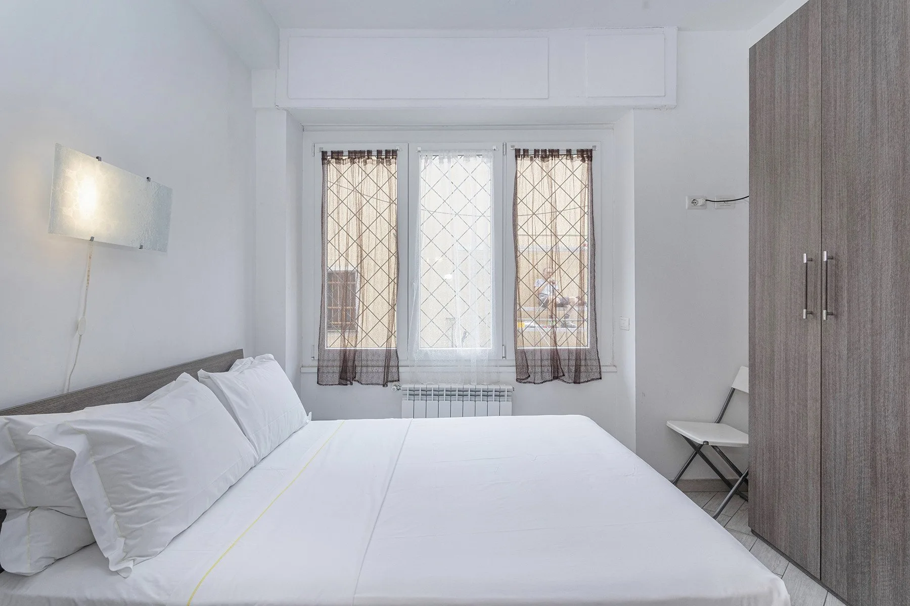 Un dormitorio luminoso con una cama blanca, una ventana y un armario.