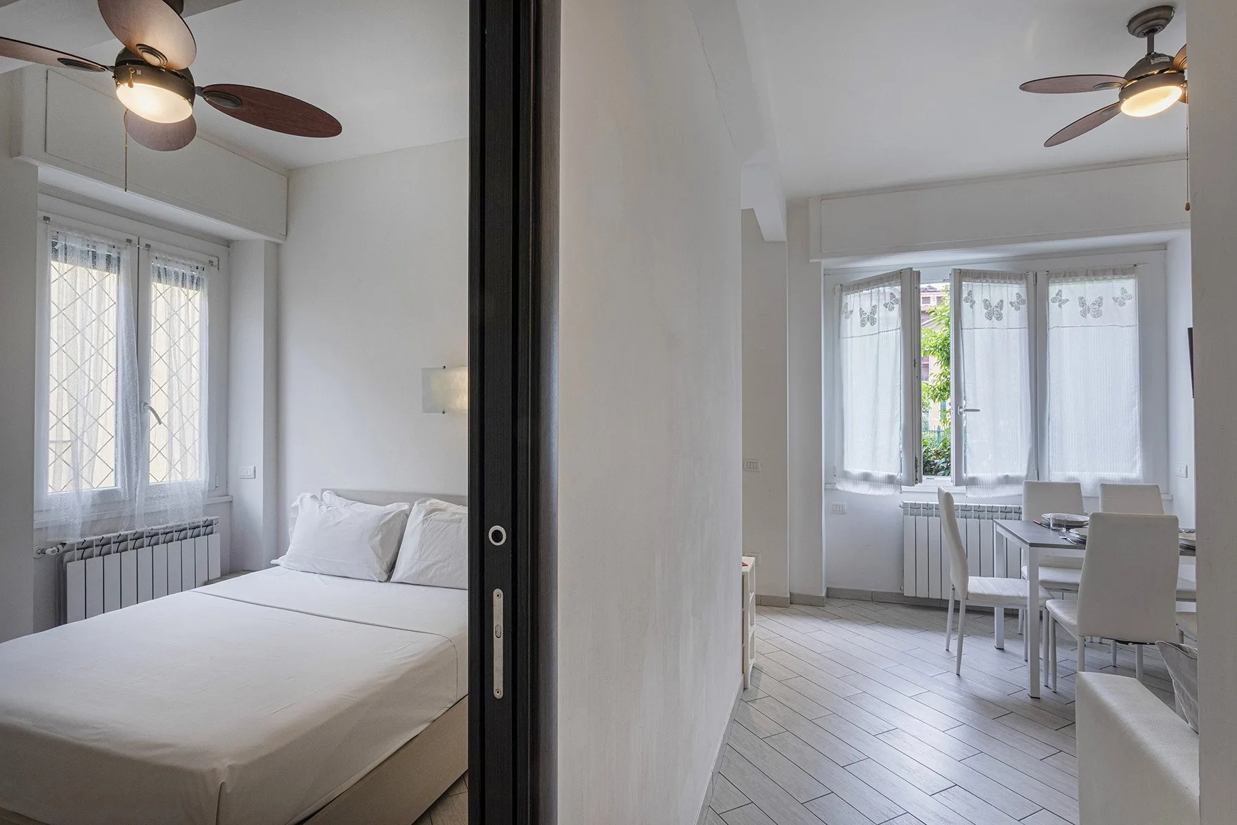 Un dormitorio se abre a un comedor, con muebles blancos y ventiladores de techo.