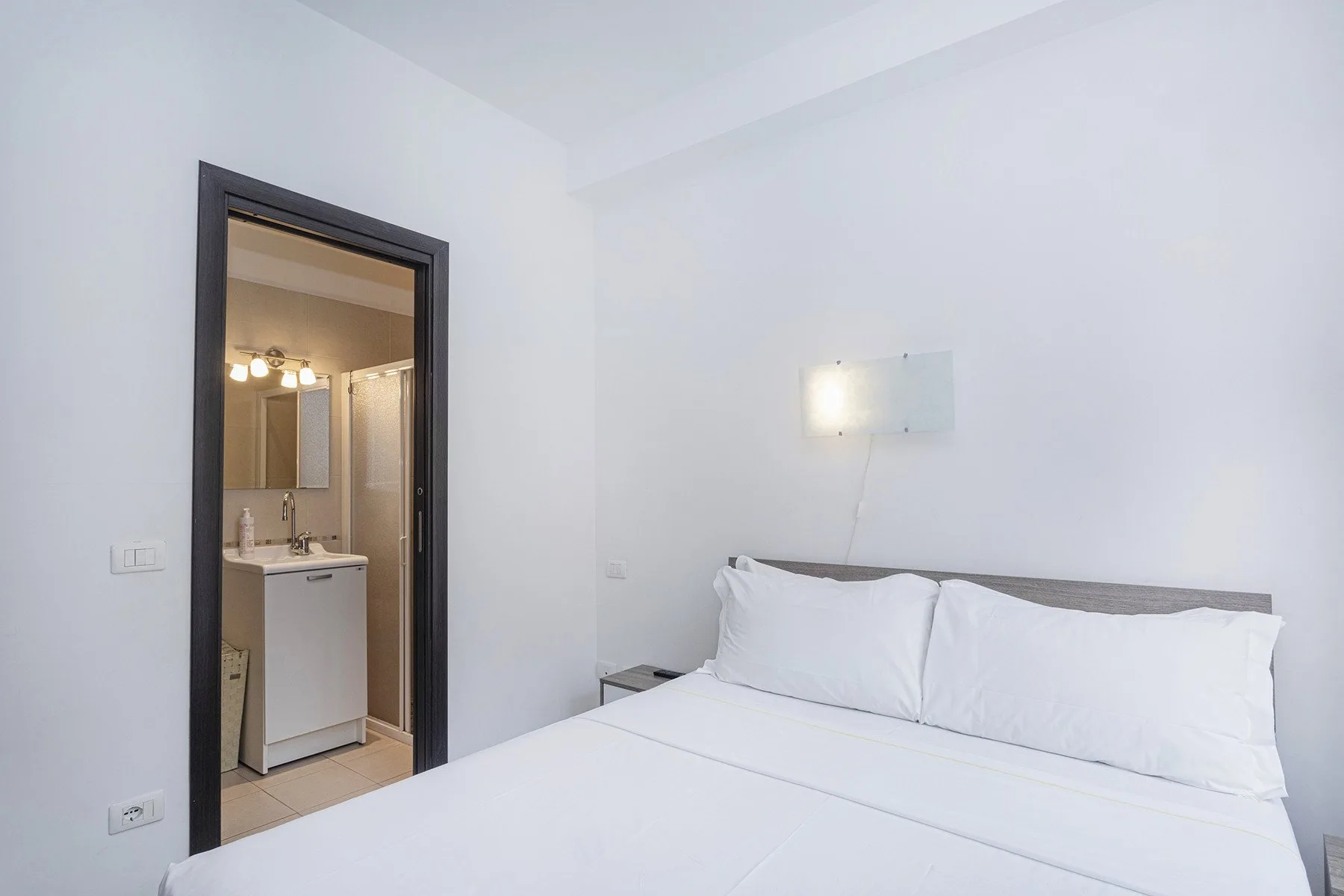 Un dormitorio con una cama tendida y una puerta abierta hacia un baño.