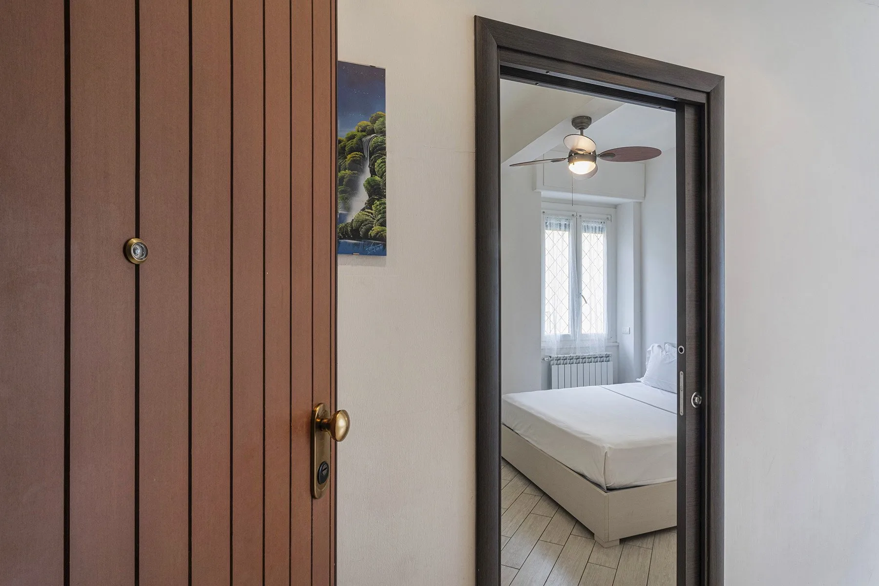 Se ve un dormitorio a través de una puerta abierta, con una cama bajo un ventilador de techo.