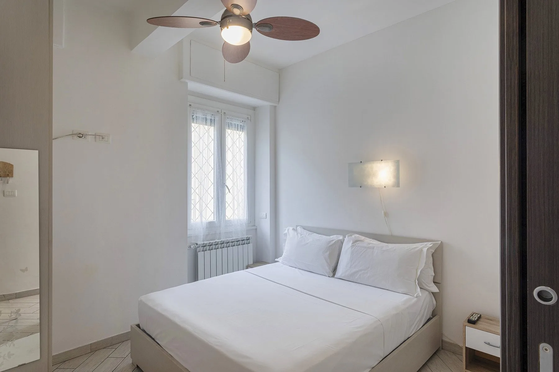 Un dormitorio con una cama bien arreglada bajo un ventilador de techo.