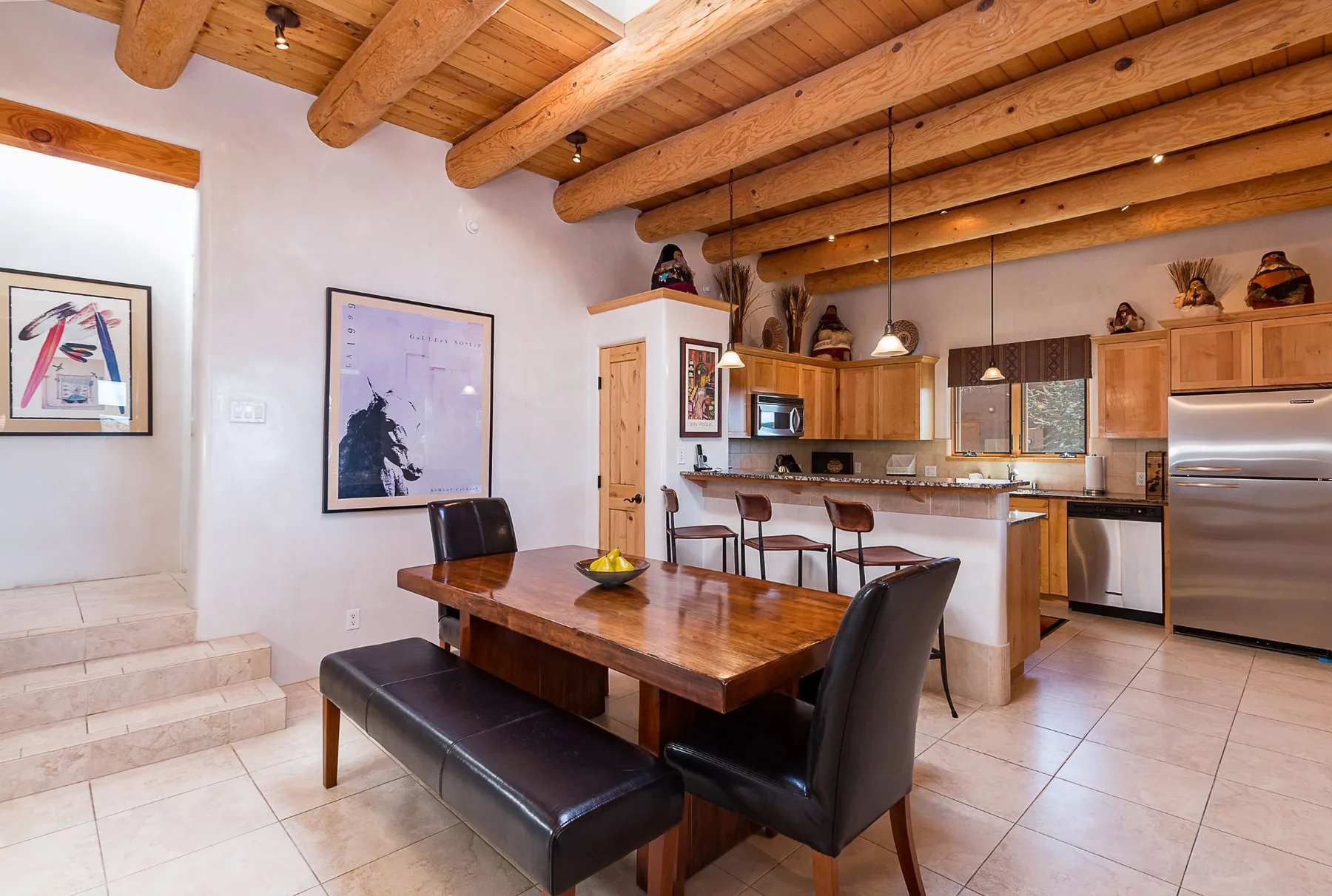 An open dining and kitchen area with a wooden table beneath exposed beams.