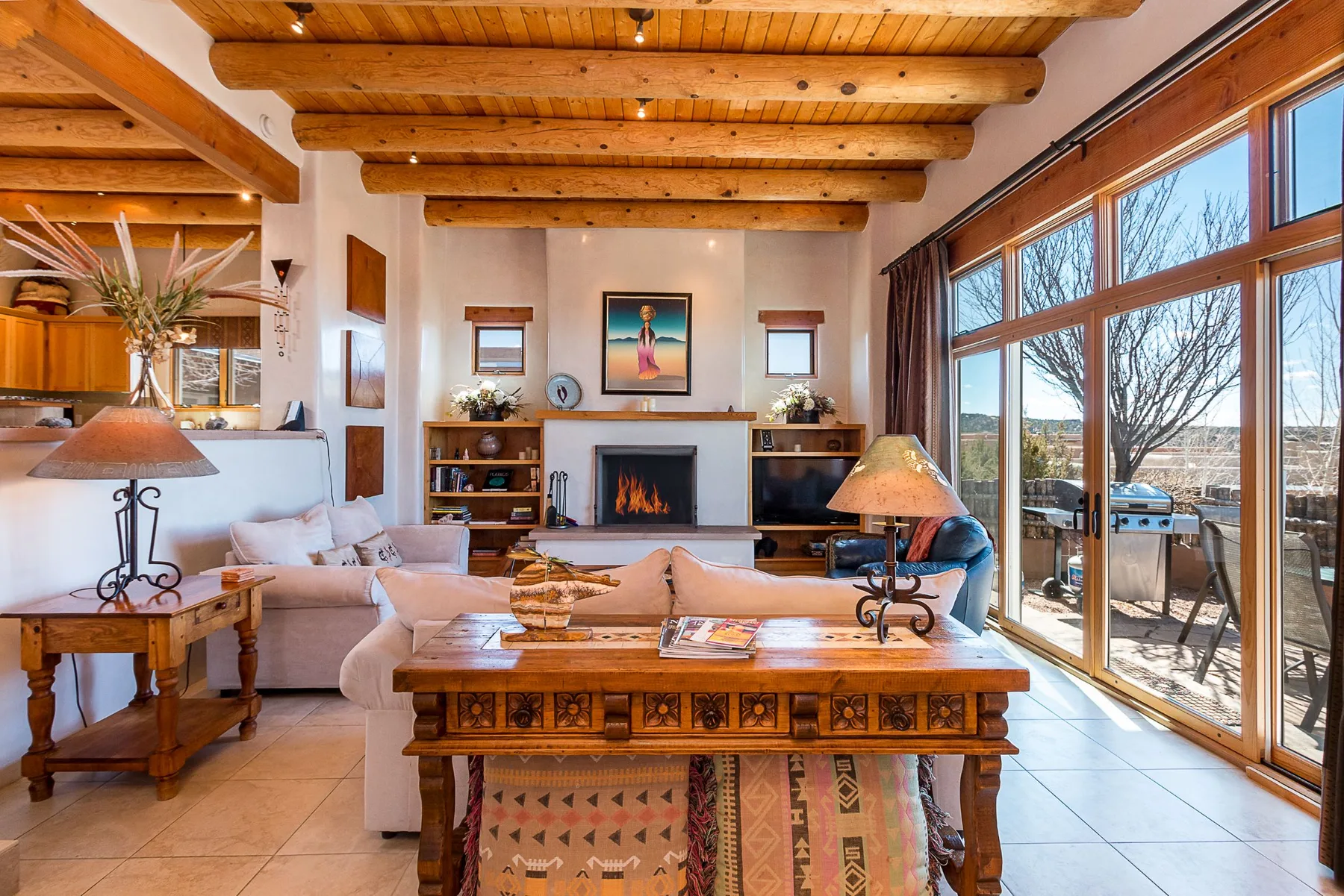 A living room with exposed wooden ceiling beams and large windows.