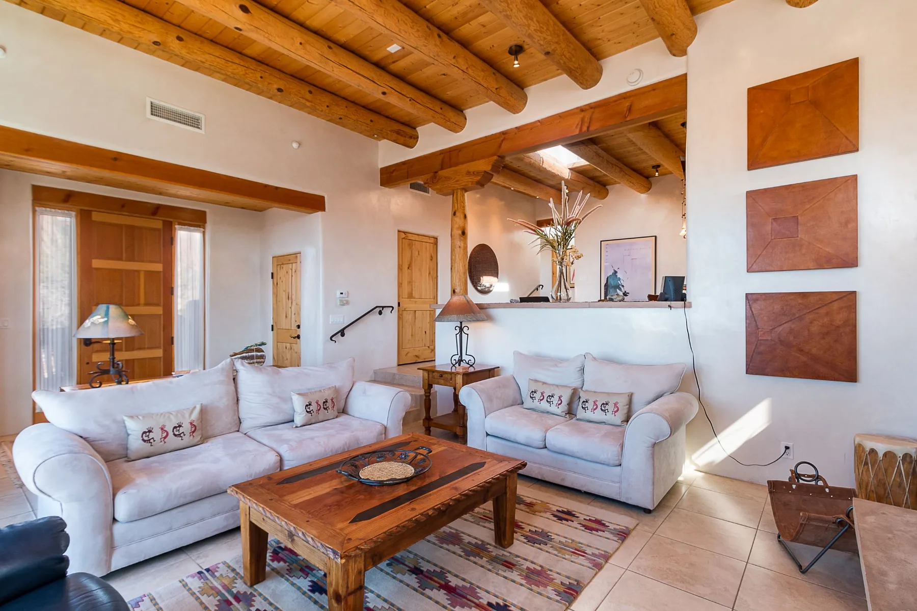 A living room with pale seating, a wooden coffee table, and exposed timber ceiling beams.