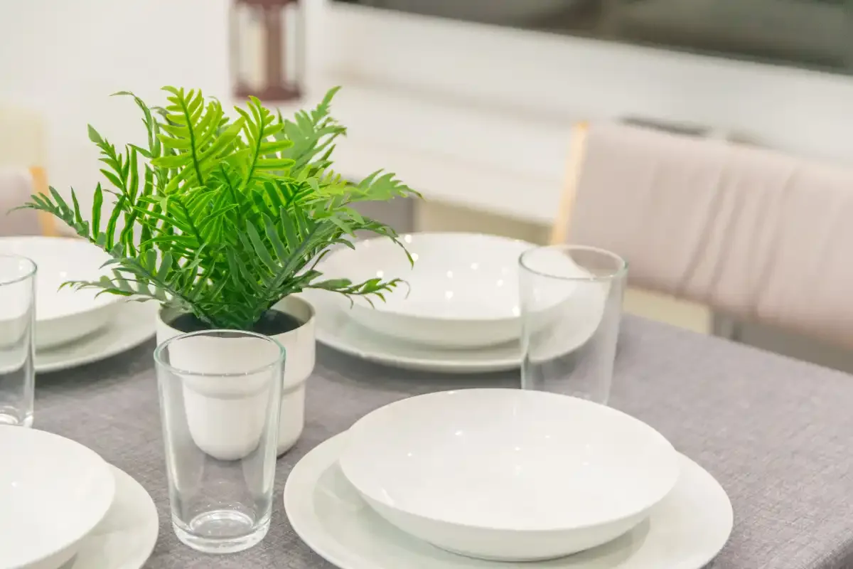 Una mesa de comedor está puesta con platos blancos y una planta en maceta.
