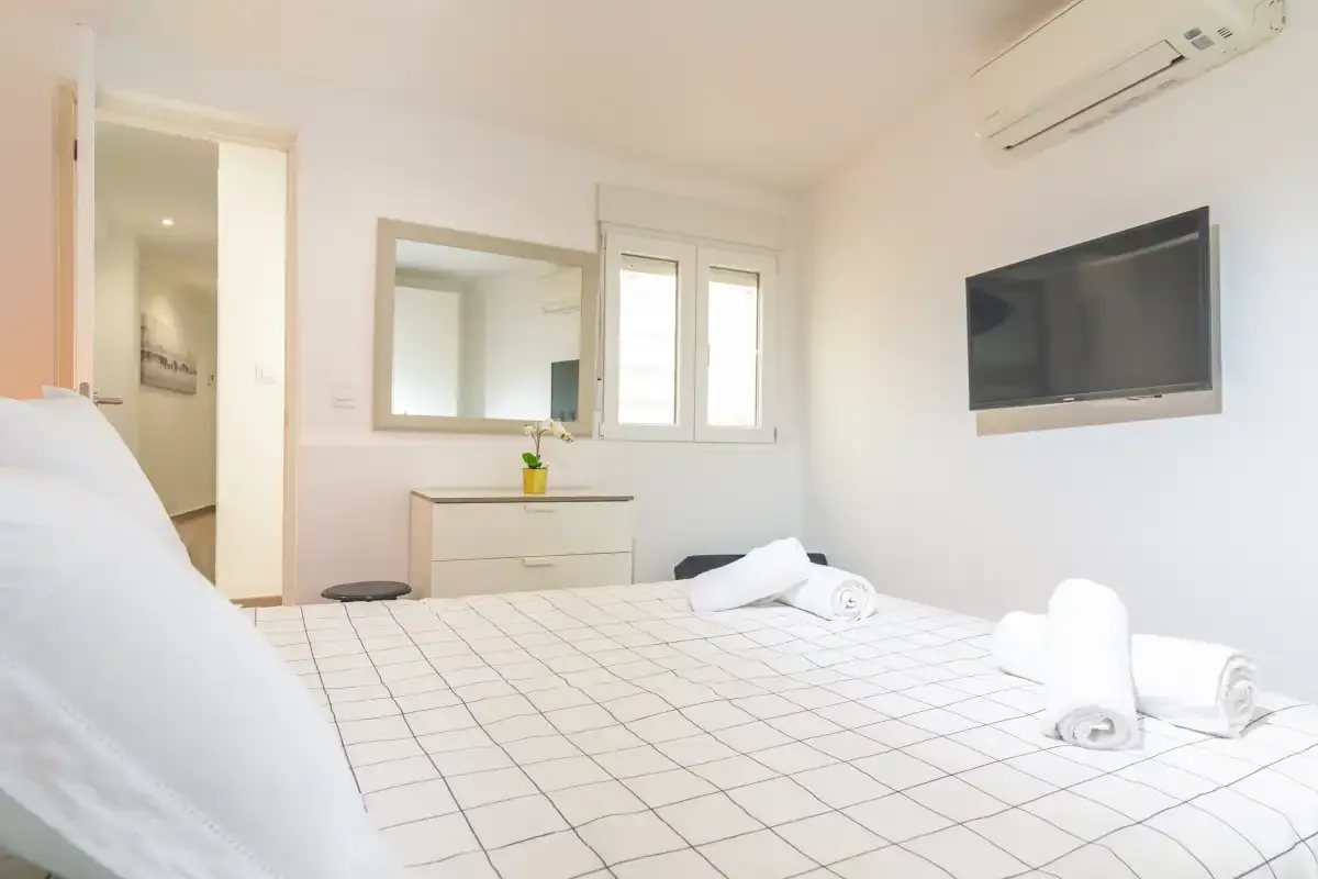 Un dormitorio con una cama, una cómoda, una ventana y un televisor de pared.