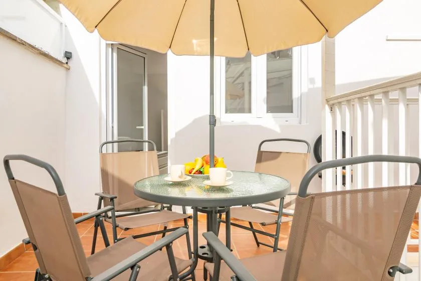 Una zona de comedor en un patio al aire libre, con mesa, asientos y una sombrilla grande.