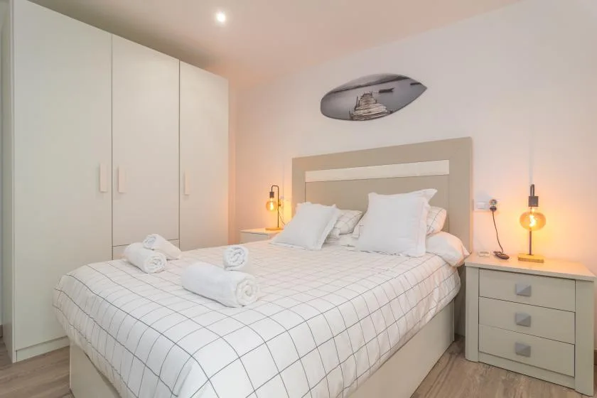 Un dormitorio con una cama bien hecha, armarios blancos y mesitas de noche.
