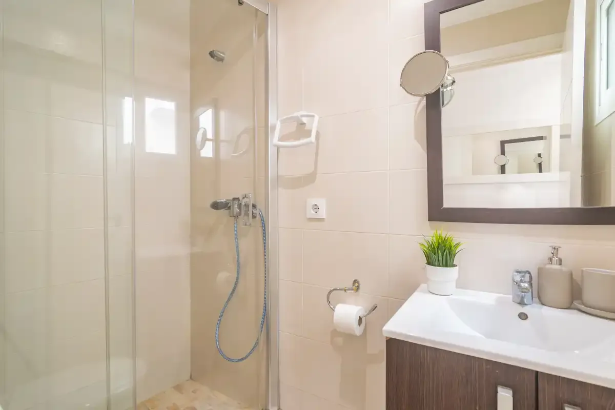 Un baño luminoso tiene una ducha de vidrio y un lavabo blanco.