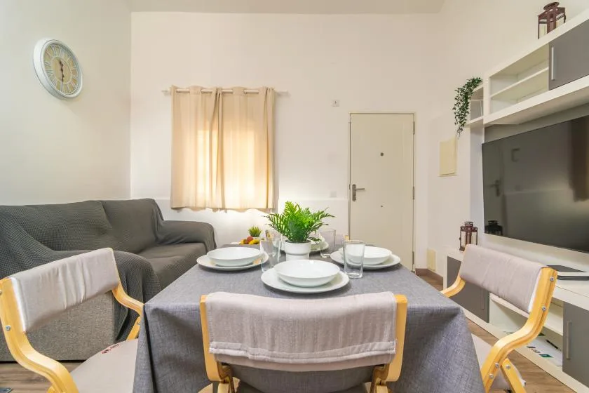Comedor con una mesa puesta junto a un sofá gris y una ventana con cortinas.