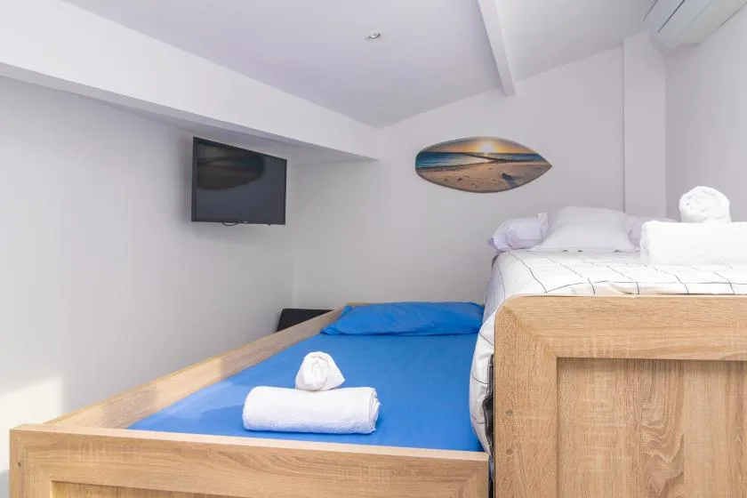Un dormitorio con una cama azul, ropa de cama blanca y un televisor en la pared.