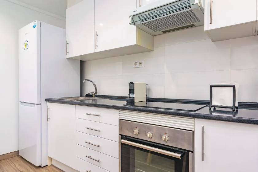 Una cocina luminosa con gabinetes blancos, un refrigerador y un horno.