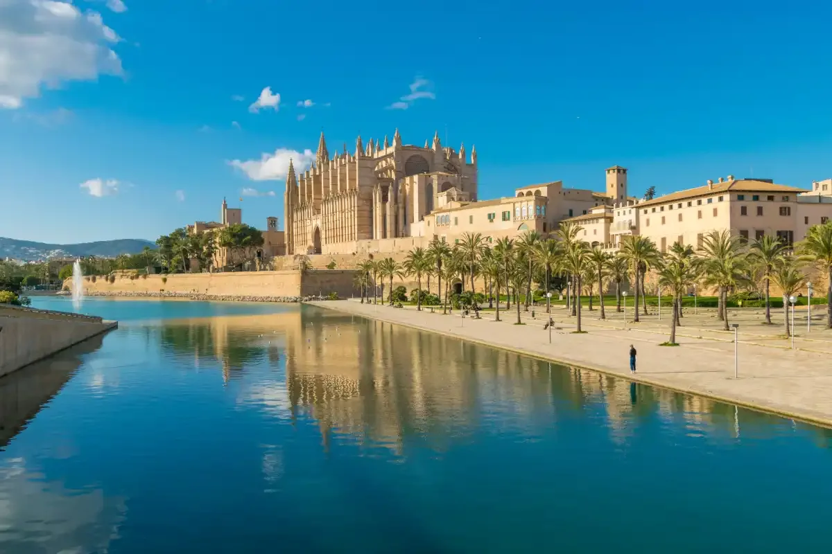 Una gran catedral gótica se alza junto a un paseo marítimo y aguas tranquilas.