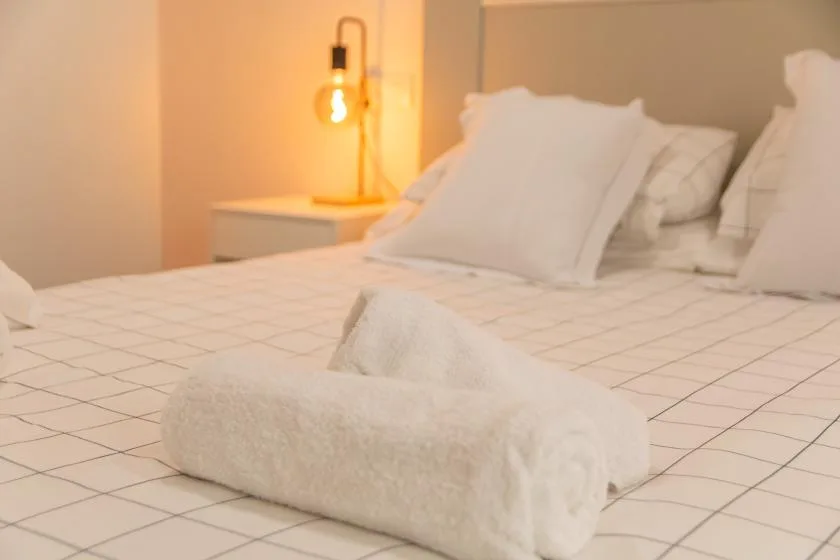 Un dormitorio con ropa de cama blanca y una toalla doblada sobre la cama.
