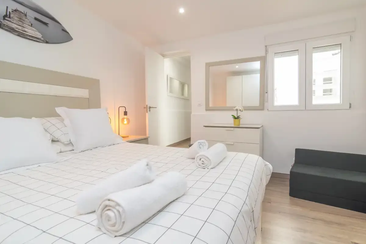 Un dormitorio luminoso con una cama tendida y una ventana.