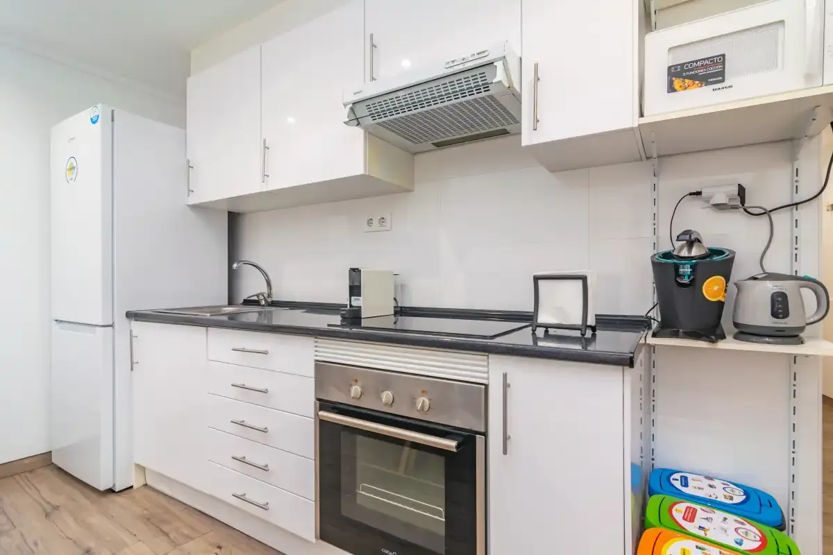 Una cocina compacta con armarios blancos, una encimera y un horno integrado.
