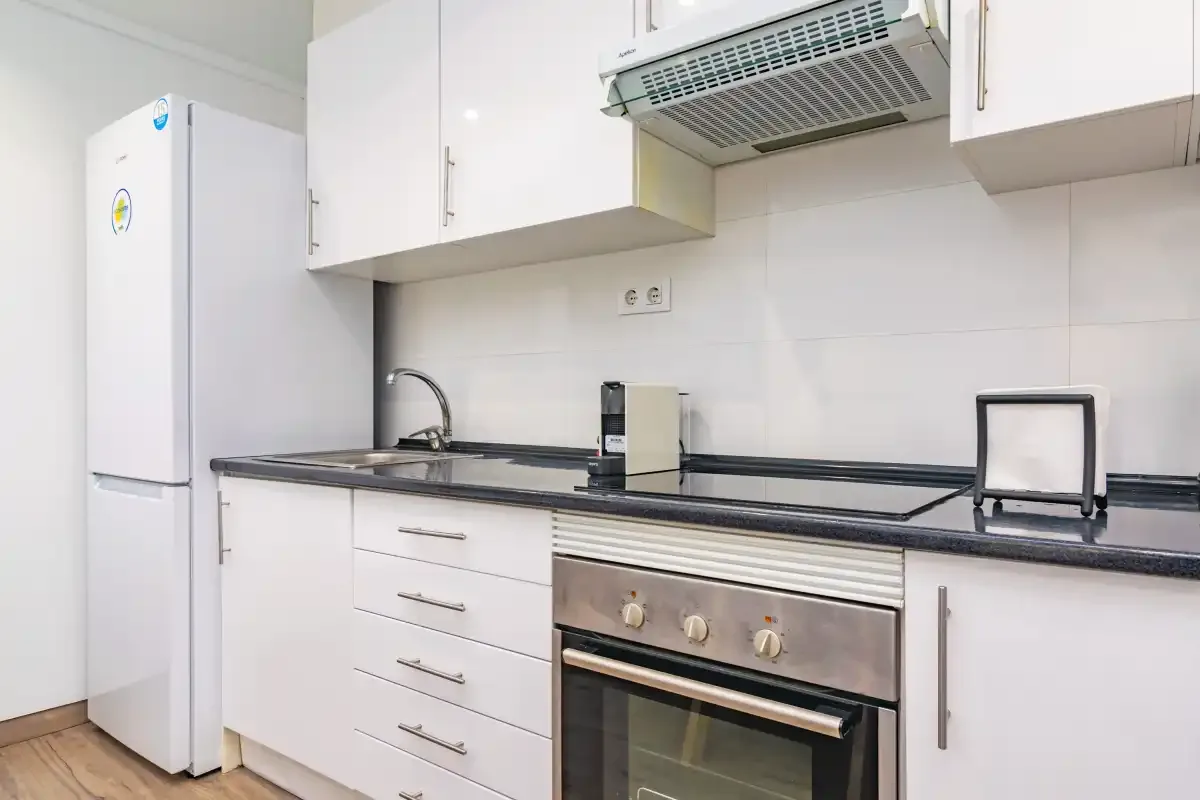 Una cocina luminosa con armarios blancos, una encimera y electrodomésticos integrados.