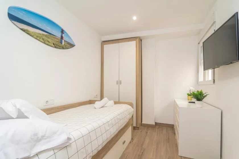 Un dormitorio con una cama individual, un armario y un televisor en la pared.