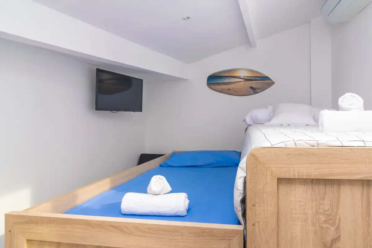 Un dormitorio con dos camas, ropa de cama azul y un televisor en la pared.