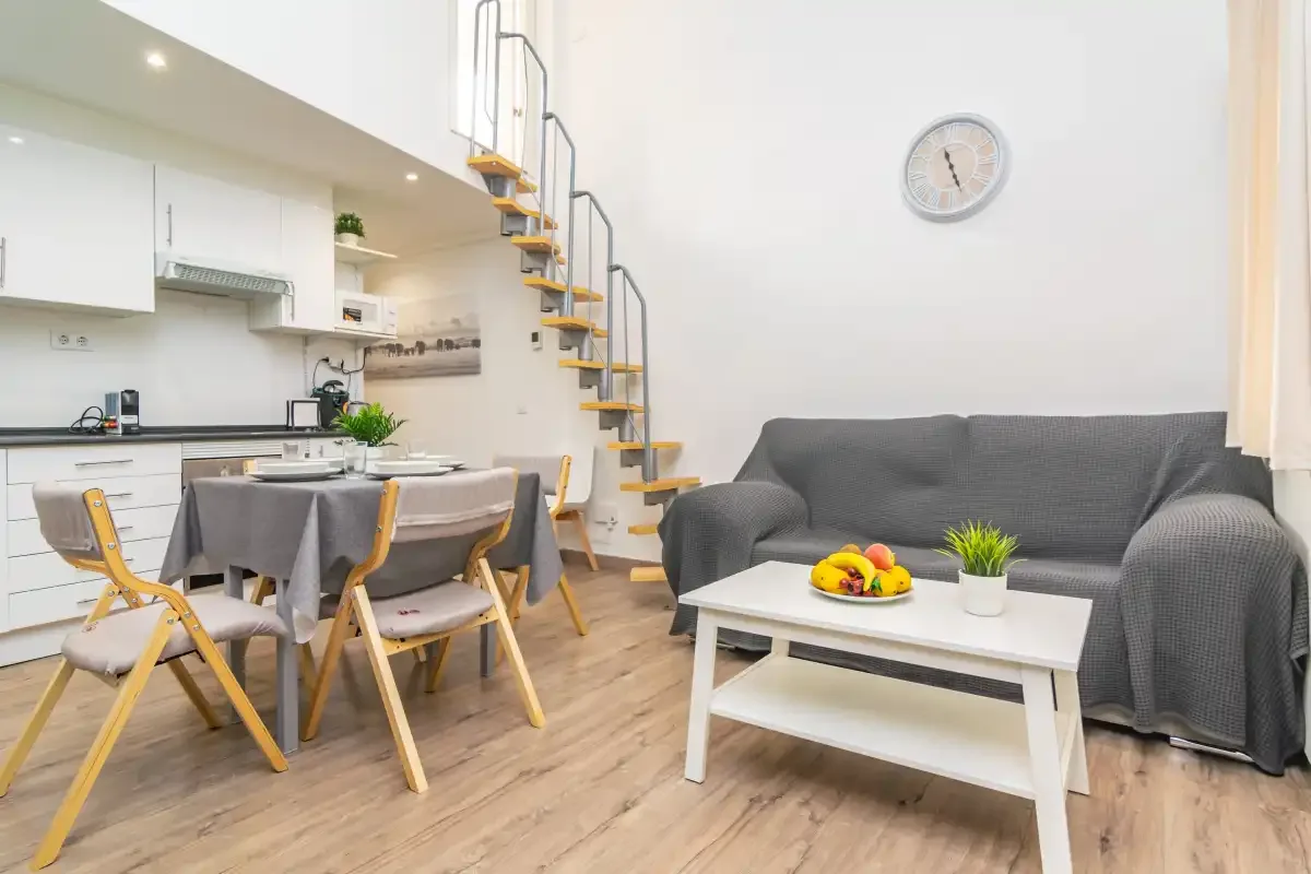 Una luminosa sala de estar y comedor con un sofá gris y una mesa.