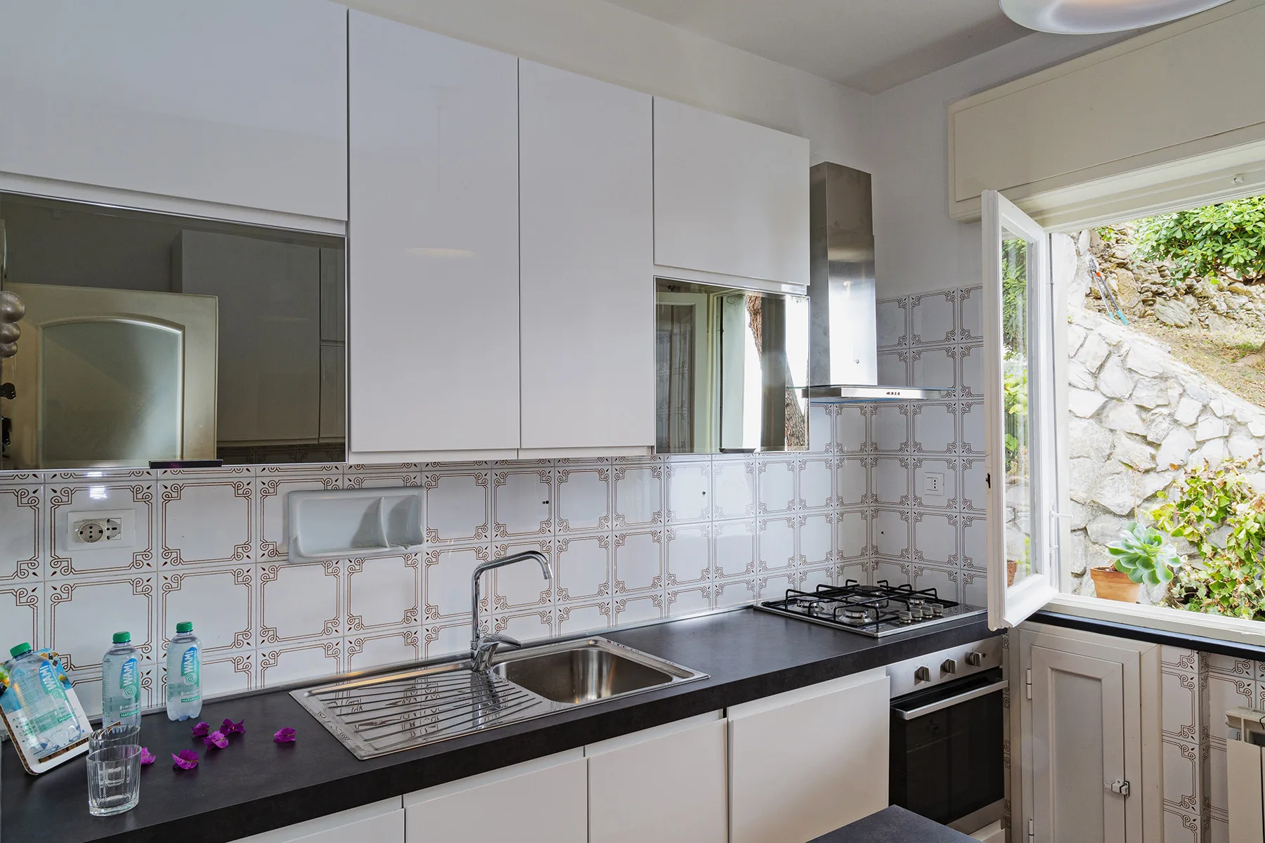 Una cocina luminosa con encimera oscura, fregadero y cocina de gas.
