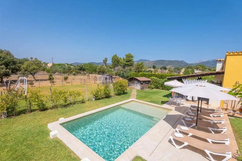 An outdoor swimming pool beside a patio with lounge chairs and an open landscape beyond.