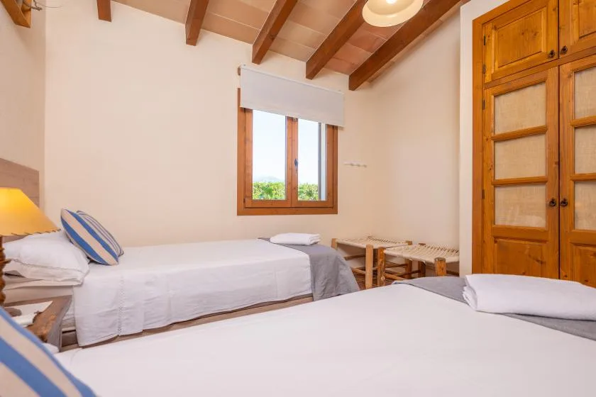 A bedroom with two beds, wooden ceiling beams, and a window.