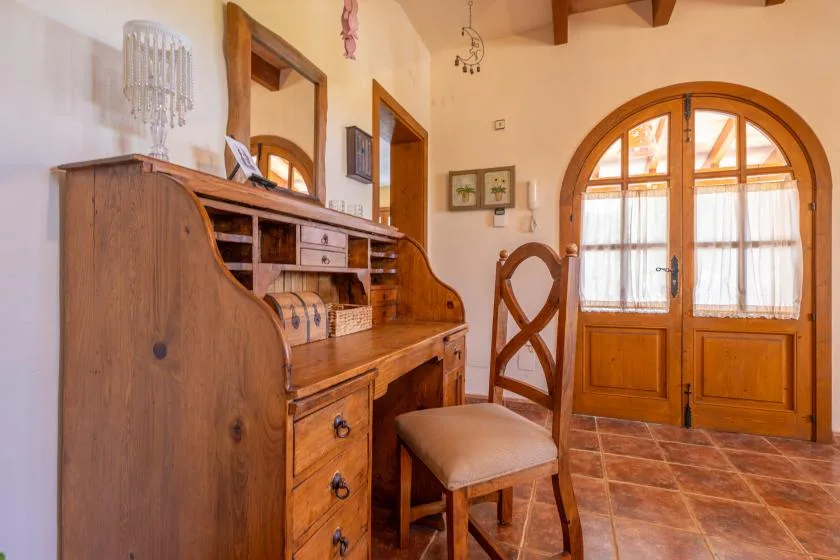 A wooden writing desk and chair sit beside an arched glass-paneled doorway.