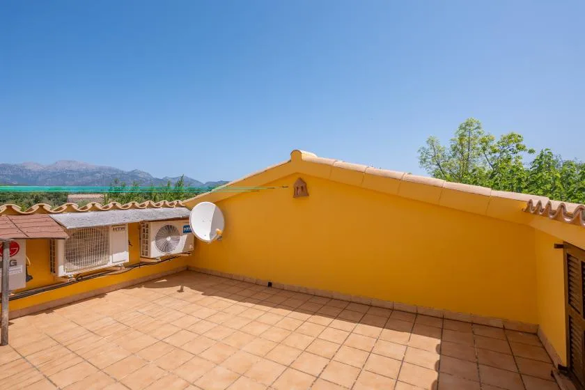 A sunny tiled rooftop terrace bordered by bright yellow walls, with distant hills beyond.