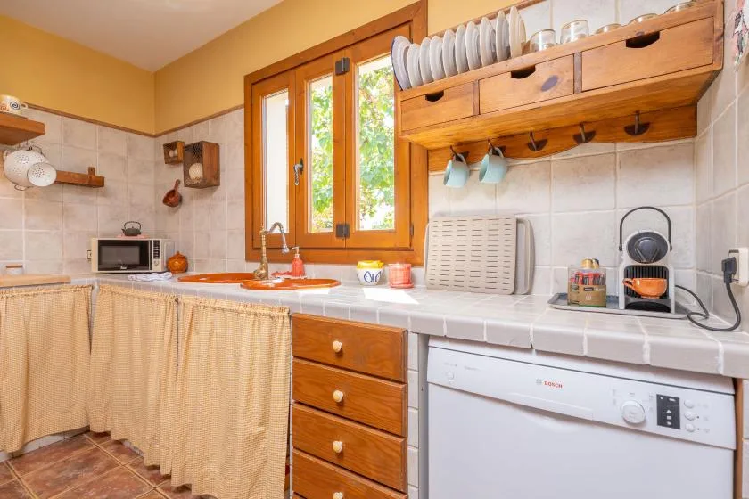 A kitchen with a tiled counter, wooden cabinets, and a window overlooking greenery.
