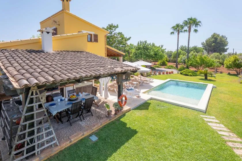 A sunny backyard with a swimming pool beside a shaded outdoor dining area.