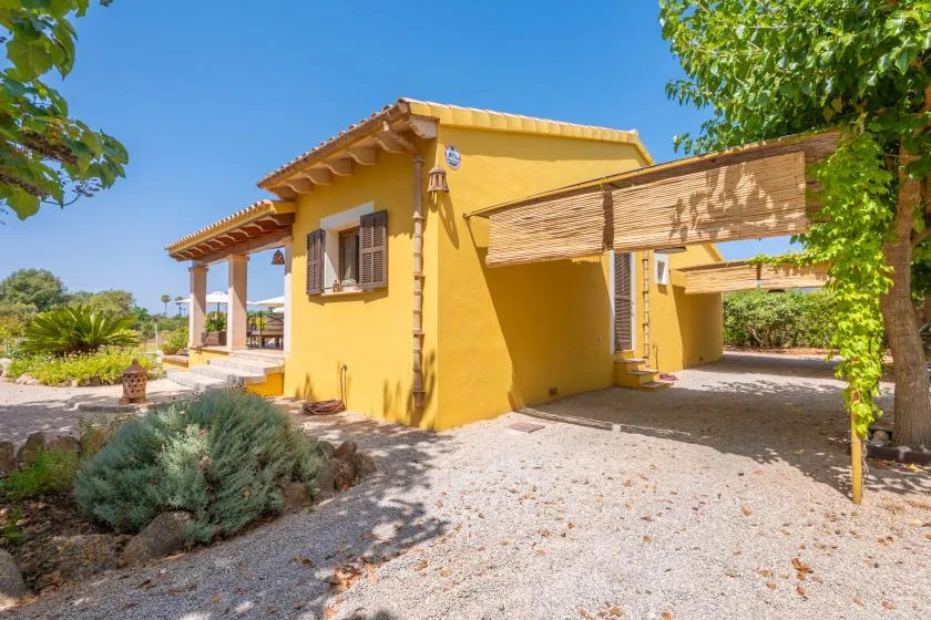 A yellow house with a shaded driveway beneath a wooden pergola.