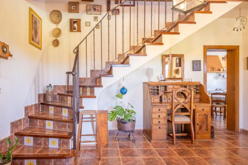 A tiled interior features a wooden staircase and a desk beneath it.