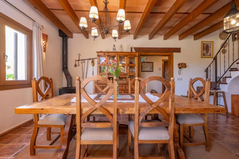 A dining room with a long wooden table and chairs beneath exposed ceiling beams.