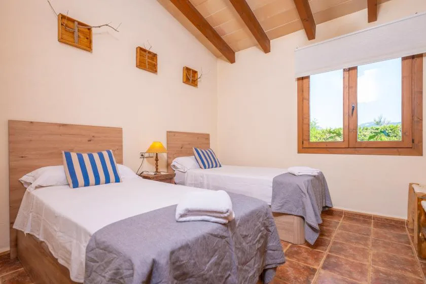 A bedroom with two beds, gray bedding, and a wooden-framed window.