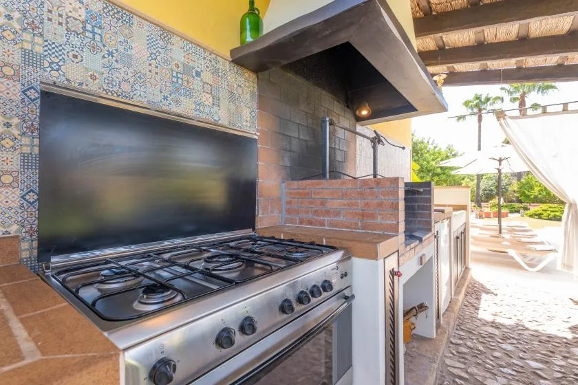 An outdoor kitchen with a gas cooktop and brick backsplash overlooks a sunny patio.