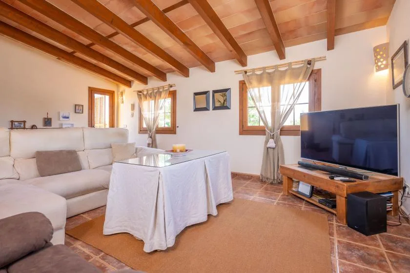 A living room with seating, a table, and a television beneath exposed wooden beams.