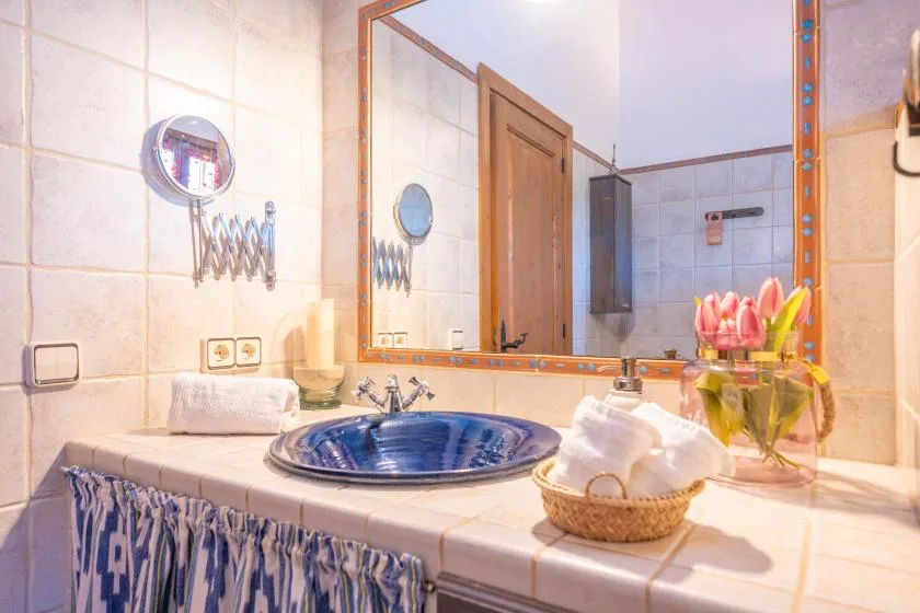 A tiled bathroom vanity with a blue basin, mirror, and flowers.