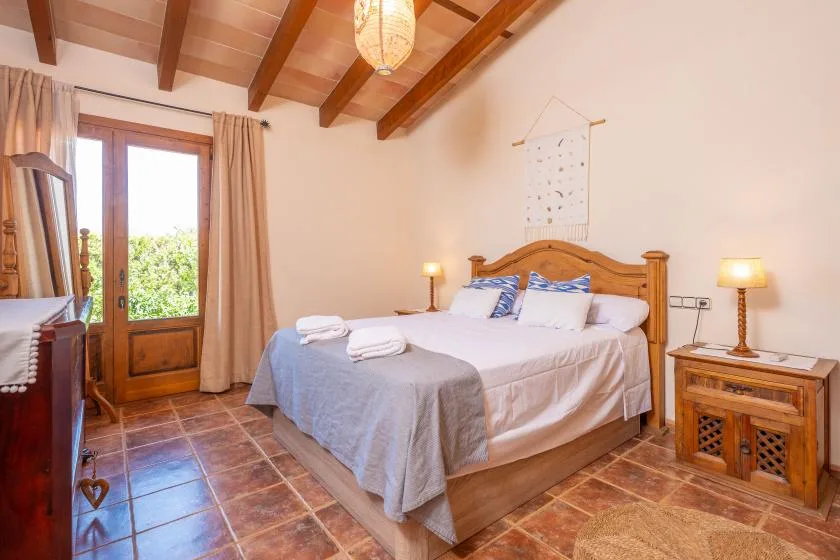 A bedroom with a double bed, exposed wooden ceiling beams, and a glass-paneled door.